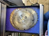Photo shows a drawer containing six circular saw blades, varying in size and condition. One blade is rusted and others show wear marks. The blades mostly measure around 10 inches.