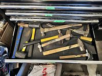 View of open drawer containing 11 assorted hammers of various sizes and handle types in a large tool chest.