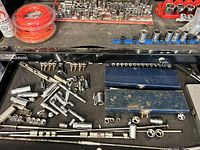 Top view of open tool chest drawer containing assorted ratchets, sockets, extension bars, and two metal tool boxes.
