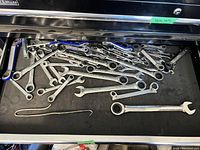 Drawer with a large assortment of combination wrenches and open-end wrenches of various sizes laid flat on a black surface inside a tool chest drawer.
