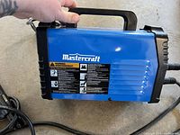 Side view of the blue Mastercraft arc stick welder showing brand label and warning instructions.