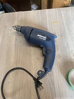 Mastercraft branded corded reversible driver/drill in blue plastic casing laid flat on a wooden surface with visible power cord.