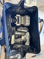 Top view inside the black carry bag showing cordless drill, two batteries, and charger neatly placed inside.