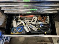 Top-down view of open tool chest drawer containing assorted hand saws, clamps, pneumatic tool, wire wheels, hacksaw, screwdrivers, and various other small tools.