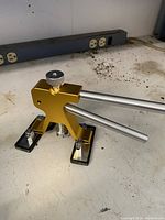 Photo showing the gold-colored dent removal tool on a workbench from a side angle, highlighting the screw knob and metal lever arms.