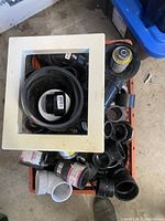Top view of milk crate filled with various black and white PVC pipes and fittings including elbows and connectors.
