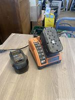 Photo of Rigid orange and black battery charger with indicator lights, one battery attached and one separate on table.