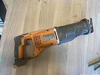 Side view of the Rigid cordless reciprocating saw showing the orange and black body, ergonomic handle, and blade clamp area.