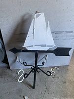 Photo of metal wind vane with white sailboat and directional markers showing condition and design details.