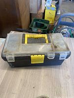 Closed black plastic toolbox with yellow latch covered in dust on wooden table