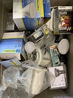 View inside tote showing metal junction boxes, packaged and loose light bulbs, light switches, and wire nuts