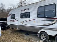 Exterior side view of white Hornet travel trailer with retracted awning and graphics