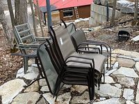 Photo showing stacked brown mesh metal patio chairs and gray slatted metal chairs beside the table outdoors on stone tile patio.