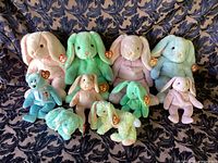 Front view of all 10 Ty Beanie Babies including 4 large bunnies and 6 smaller bunnies and bear, arranged on a patterned fabric background.