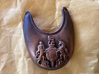 Front view of the metal gorget showing the central embossed shield with lion and unicorn heraldic figures.