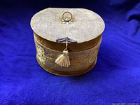 Round antique fabric-covered jewelry/trinket box with embroidered gold designs and closed lid showing tassel pull.