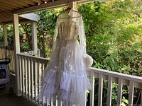 Photo of the vintage wedding dress hanging on a porch railing showing the full dress length and tulle layers.