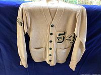 Front view of vintage 1954 cream colored cardigan with green buttons and '54' patch on left chest, showing knit texture and front pockets.