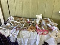 Full view of the 41-piece lot of vintage handmade embroidered and crocheted linens spread over a table, showing variety of items including doilies and towels with intricate patterns and colorful crochet edges.