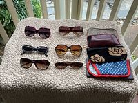 All six sunglasses and five cases arranged on a beige textured surface showing colors and condition.