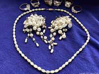 Full lot shown on dark blue fabric background including 6 rings, pearl choker necklace, and cluster faux pearl earrings.