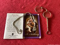 Antique foldable lorgnon glasses, St Anthony prayer card and necklace laid on red cloth