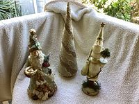 Three holiday decor items displayed: two Father Christmas figurines and one glittered gold Christmas tree on a fleece backdrop outside.