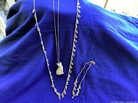 Photo showing three pieces of jewelry: a kitty cat pendant necklace, an alphabet charm necklace, and a bangle ankle bracelet laid out on blue fabric.