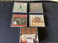 Five Elvis Costello CDs arranged on a dark surface showing all covers: My Aim Is True, This Year's Model, Elvis Costello and Burt Bacharach, Armed Forces, Girls Girls Girls 2-disc set.