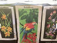 Three TelaVera branded vintage Brazilian needlepoint and cross stitch fabric patterns displayed side by side. Middle pattern features a large colorful parrot; flanking patterns show different floral designs. Original Brazilian price tags attached.