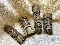 Four wooden carvings placed on a fabric surface, showing front faces with carved detailed expressions.