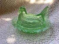 Light green glass nesting hen dish with the hen cover placed on the base dish, photographed from front left angle on carpet surface under natural light.