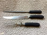 Three carving utensils (knife, fork, sharpener) laid out on beige carpet.