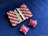 Set of vintage red jasper oval clip-on earrings with rhinestone accents and wide beaded wrist cuff on blue fabric background.