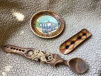 Photo of all three Romanian folk art pieces displayed on carpet: hand painted plate, carved wooden spoon, and small dish