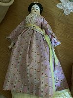 Front view of the porcelain doll in pink floral dress on wooden surface