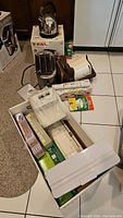 Overview of multiple kitchen appliances including T-Fal toaster, kettle, Melita coffee maker, and Food Saver vacuum packaging system with rolls in boxes and packaging.