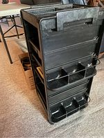 Front side of the black rolling cart showing multiple compartments and two wire holders on the side