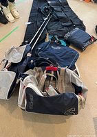 Photo of various ski equipment bags and ski poles arranged on floor showing brands and types.