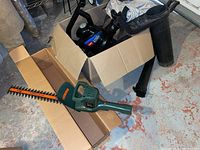 Black & Decker 16 inch electric hedge trimmer with green handle and orange blade, shown outside box.