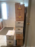 Stack of eight labeled cardboard boxes containing books, some boxes with 'Shell Cleaning Solvent' logos, stacked near a door indoors.