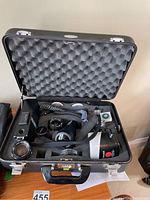 Open black Halliburton camera case showing contents including Canon lenses and a Graflex strobe flash.