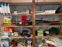 Garage shelf with hoses, spray wands, red bench vise, battery charger, coil hoses, and other garage maintenance items.