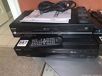 Front view of Toshiba SDV32KKC DVD/VHS combo player with two remotes and power cable on top.