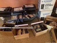 Overall view of four boxes with stacked electronics, cords, cables, and boxed Pioneer speakers