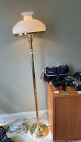 Full view of brass floor lamp showing twisted brass pole, round base, and white opaque glass shade with brass trim.