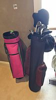 Two golf bags standing side by side. One is pink with black and gray, the other black with red accents holding clubs.