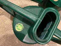 Close-up of green metal Haws watering can showing oval top opening and logo badge on lid