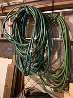 Overview of several garden hoses hanging on wall hooks.
