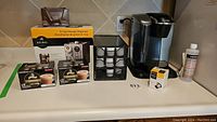 Keurig coffee machine with boxes of coffee capsules, K-Cup dispensers, descaling solution on kitchen counter.